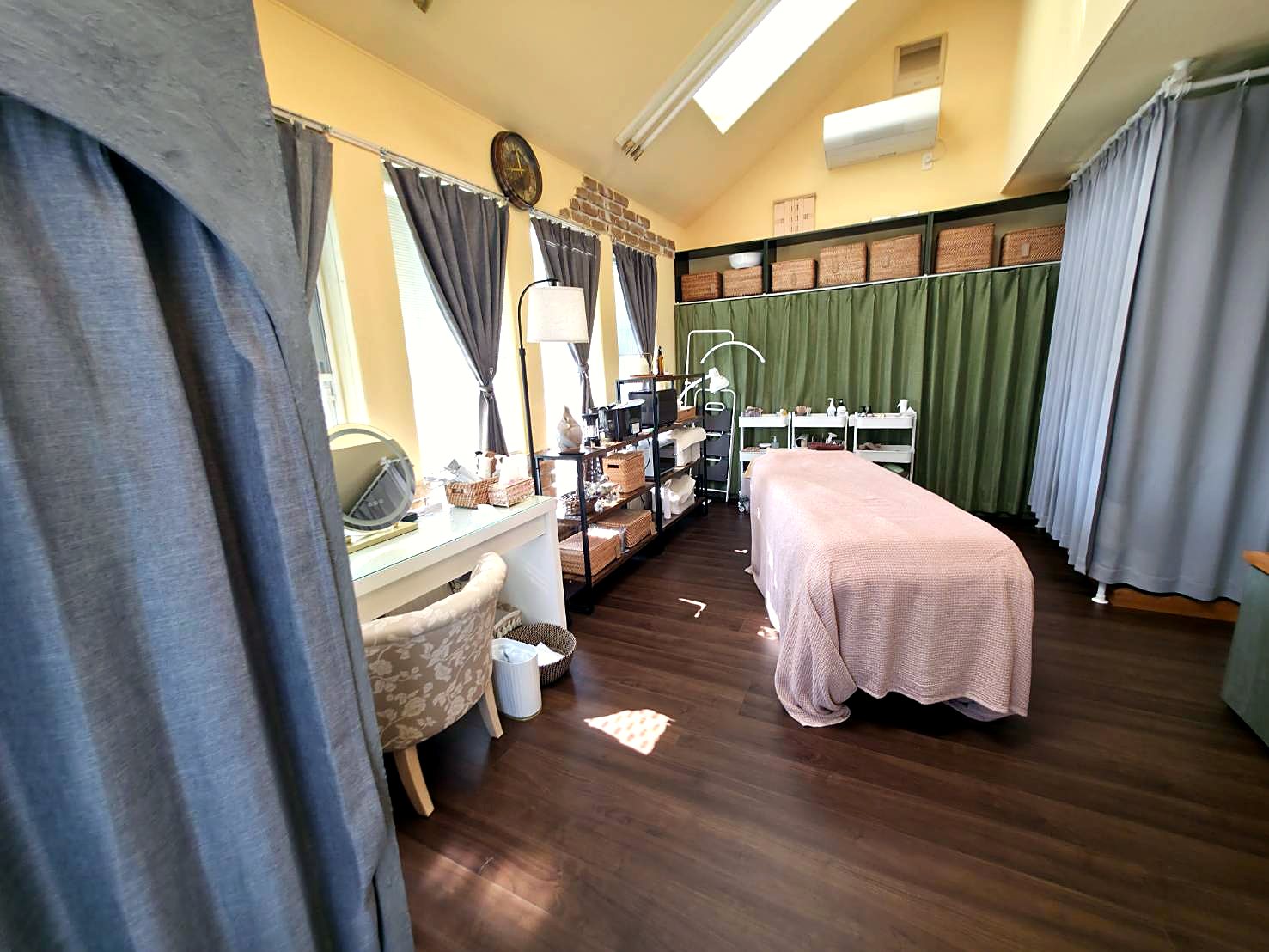 天窓から昼の光が入るお部屋。施術ベッドと白いドレッサー、緑のカーテン